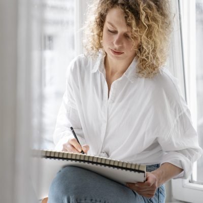 young-woman-drawing-home-near-window